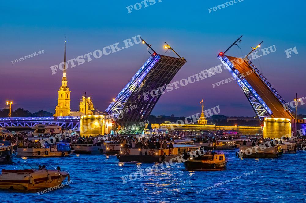 Это фотография разведённого Дворцового моста в Санкт-Петербурге. Вокруг моста собралось множество судов, что указывает на популярность этого зрелища среди жителей и гостей города. Фото идеально подходит для туристических брошюр, статей о знаменитых местах Санкт-Петербурга или как визуальный материал, демонстрирующий ночную жизнь города.